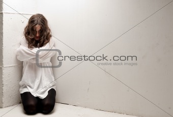 Young insane woman with straitjacket on knees looking at camera 