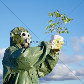 Man in chemical suit and gas mask with plant in hands