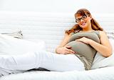 Smiling beautiful pregnant woman lying on  sofa and holding her belly.
