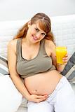 Smiling beautiful pregnant woman sitting on sofa with glass of juice  in hand
