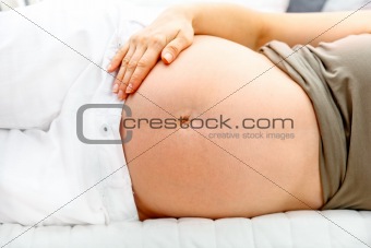 Pregnant  female lying on sofa and holding her belly. Close-up.
