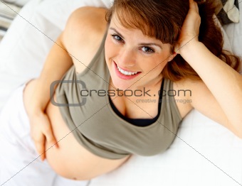 Smiling beautiful pregnant woman relaxing on couch and  holding her belly.
