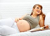 Smiling beautiful pregnant woman relaxing on couch with book.

