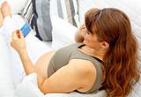 Beautiful pregnant female with mobile phone and credit card on sofa
