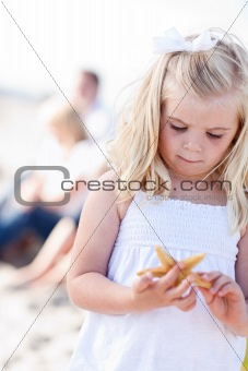 Adorable Little Blonde Girl with Starfish at The Beach.
