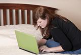 Brunette woman works from home in her bed on her bright green laptop computer.
