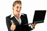 Smiling modern business woman holding laptop and showing thumbs up gesture
