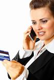 Friendly modern business woman holding credit card and talking on mobile phone
