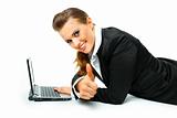 Smiling modern business woman laying on floor with laptop and showing thumbs up gesture
