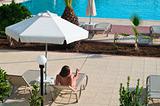 A beautiful young girl in a bikini sunbathing on a lounger near the hotel swimming pool under parasol