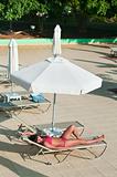A beautiful young girl in a bikini sunbathing on a lounger near the hotel swimming pool under parasol