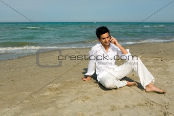 Man with mobile phone sitting in the sand at the beach