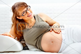 Smiling beautiful pregnant female relaxing on sofa and  holding her belly.

