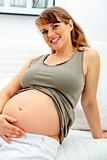 Happy beautiful pregnant woman sitting on sofa and touching her belly.
