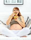 Happy beautiful pregnant woman sitting on sofa and eating fruit salad
