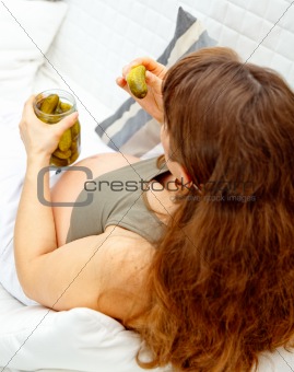 Pregnant woman sitting on sofa and  holding jar of cucumbers in hands. Closeup.
