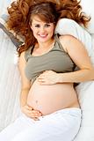 Happy beautiful pregnant woman relaxing on sofa and  holding her belly.
