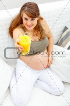 Smiling beautiful pregnant woman sitting on sofa with glass of juice  in hand.  Close-up.
