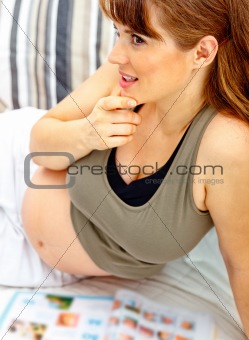 Dreaming beautiful pregnant woman relaxing on couch with magazine.
