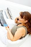 Smiling beautiful pregnant woman with mobile phone and credit card on sofa
