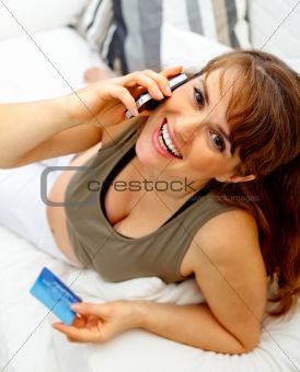 Smiling beautiful pregnant woman with mobile phone and credit card on couch
