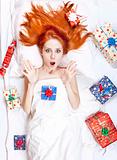 Surprised red-haired girl in bed with Christmas gifts.