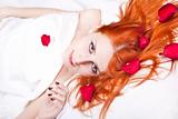 Beautiful red-haired girl in bed with rose petal. 