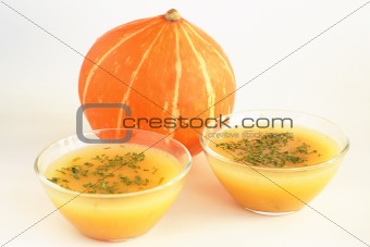 Two bowls of hot pumpkin soup and pumpkin on white background