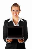 Smiling modern business woman holding laptop in hand with blank screen
