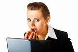 Modern business woman warily looking out from laptop and eating  apple
