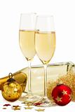 two glasses of champagne with angels hair, red and golden christmas balls in front of a champagne bottle