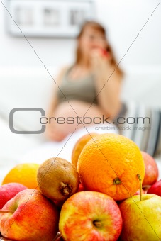 Fruit platter on table and pregnant woman sitting on sofa  in background
