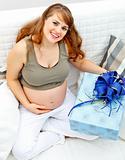 Smiling  beautiful pregnant woman sitting on couch with gift for her  unborn baby
