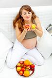 Beautiful pregnant woman sitting on sofa and enjoying fruits

