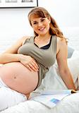 Smiling beautiful pregnant female relaxing on sofa with magazine.
