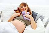 Dreaming  beautiful pregnant woman lying on sofa and holding toys. 
