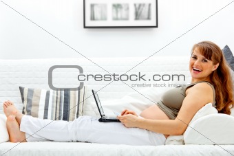 Smiling beautiful pregnant woman on sofa with the laptop and a  credit card.
