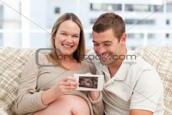 Beautiful pregnant woman showing her echography to her husband