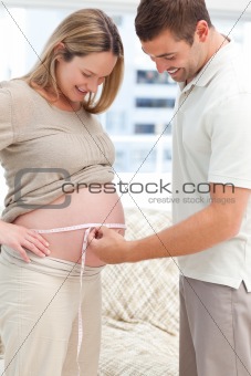 Attentive man measuring his pregnant wife's waist