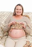 Joyful pregnant woman knitting sitting on the sofa 