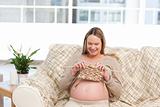 Happy pregnant woman knitting in the living-room