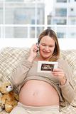 Happy pregnant woman looking at an echography while phoning 