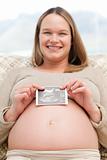 Cheerful pregnant woman holding an echography sitting on the sof
