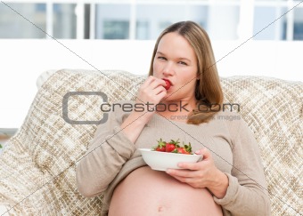Young pregnant woman eating a strawberry