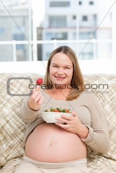 Futur mom with a bowl of strawberries sitting on the sofa