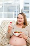 Adorable pregnant woman looking at a strawberry while relaxing