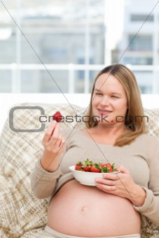 Adorable pregnant woman looking at a strawberry while relaxing