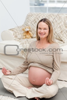 Pregnant woman doing yoga on the floor and smiling