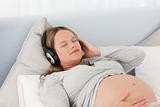 Peaceful future mother with headphones on lying on a bed