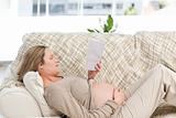 Concentrated pregnant woman reading a book lying on the couch